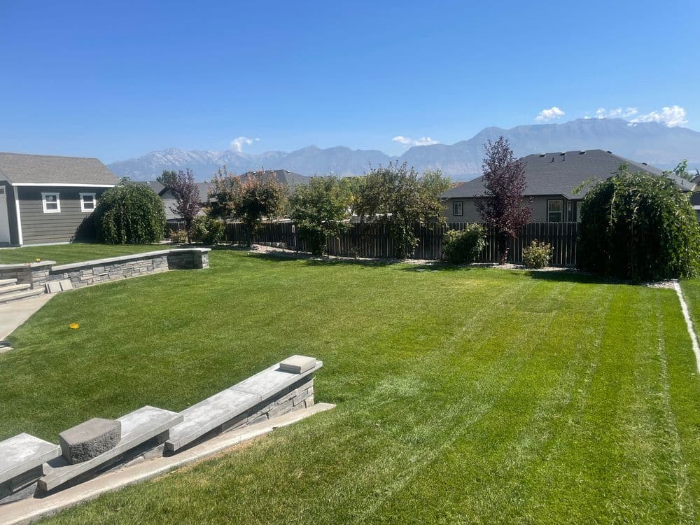 Lush green backyard with mountain views and landscaped stone features under a clear blue sky.