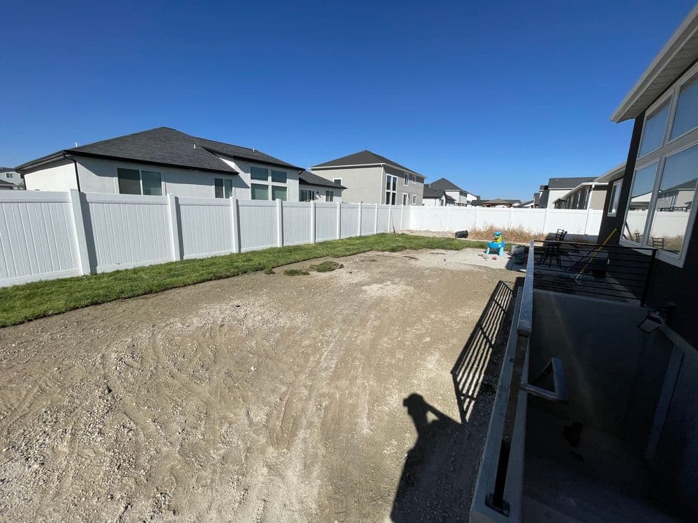 Backyard view with newly laid grass and fenced area behind modern houses under clear blue sky.