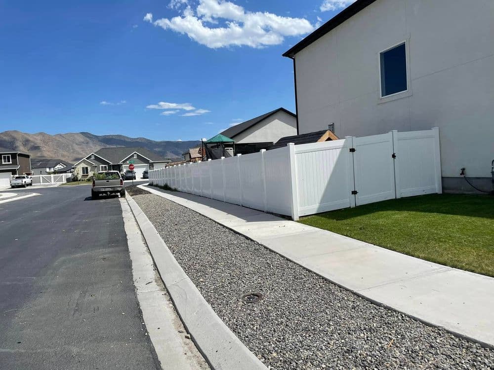 Residential street with a white vinyl fence, houses, and mountains in the background.
